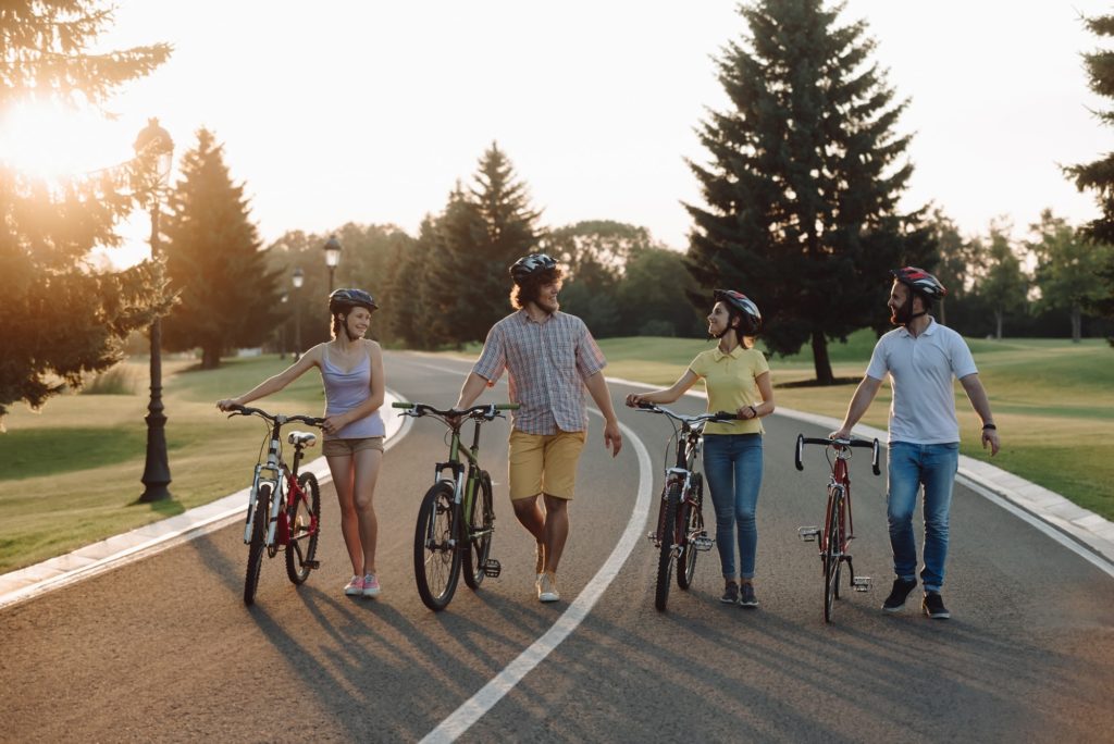 Group of cheerful cyclists walking with bicycles down the road.