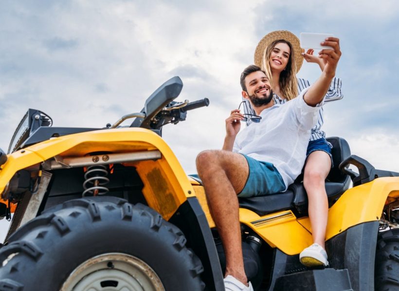 happy young couple sitting on ATV and taking selfie