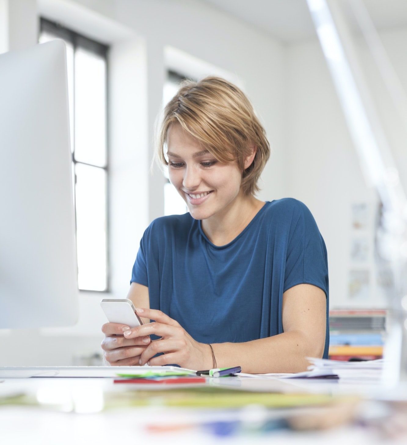 Portrait of smiling young woman using smartphone at her desk in a creative office