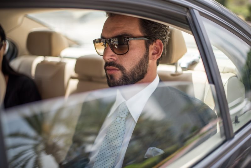 Young businessman wearing sunglasses in car backseat, Dubai, United Arab Emirates