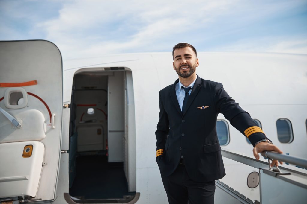 Handsome pilot standing on airstairs to plane