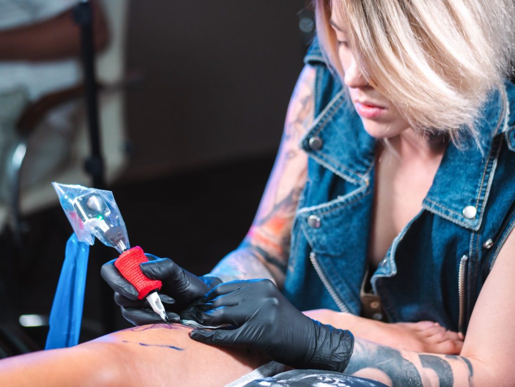 Atractive woman tattoo artist demonstrates the process of getting black tattoo with paint