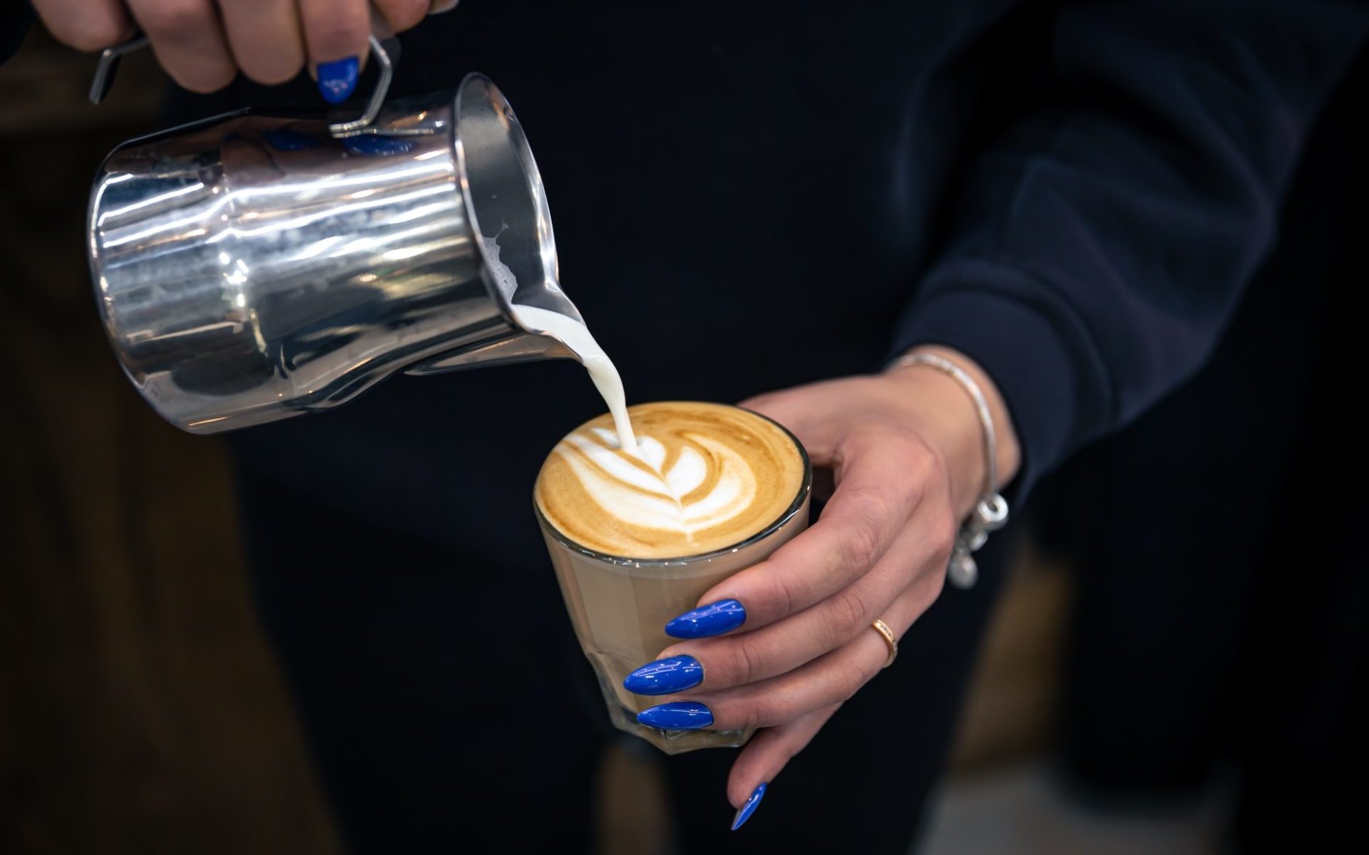 Close up hand of a woman barista pouring froth milk in espresso coffee.