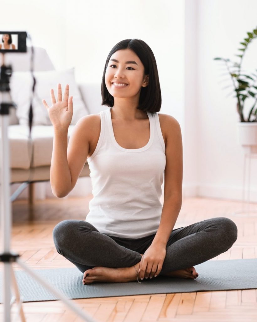 Sporty asian woman waving to camera, home training concept
