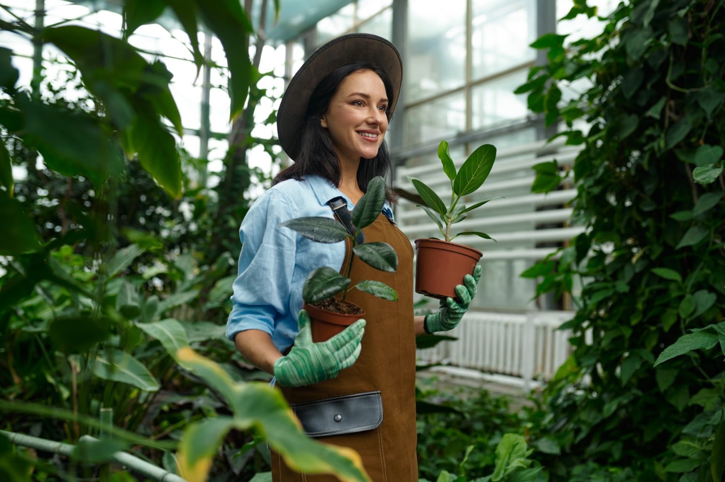Happy smiling woman gardener planting flower in greenhouse garden