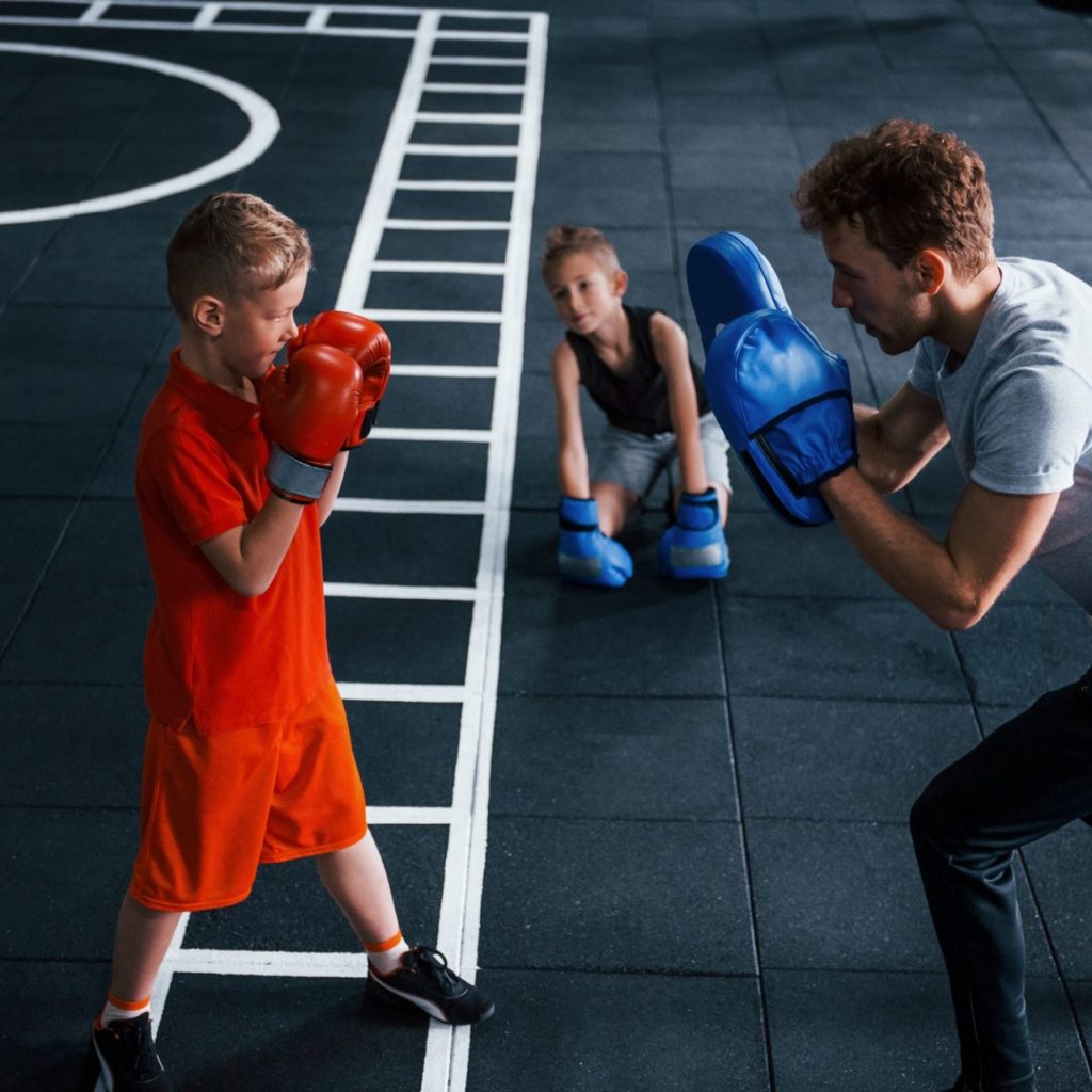 Young trainer teaches kids boxing sport in the gym