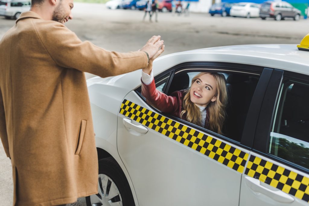 cheerful young couple giving high five and smiling each other, girl sitting in taxi and man standing