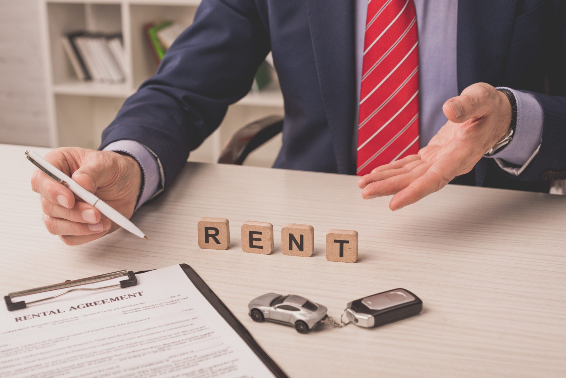 cropped view of bearded agent pointing with hand at wooden cubes with rent lettering near car key