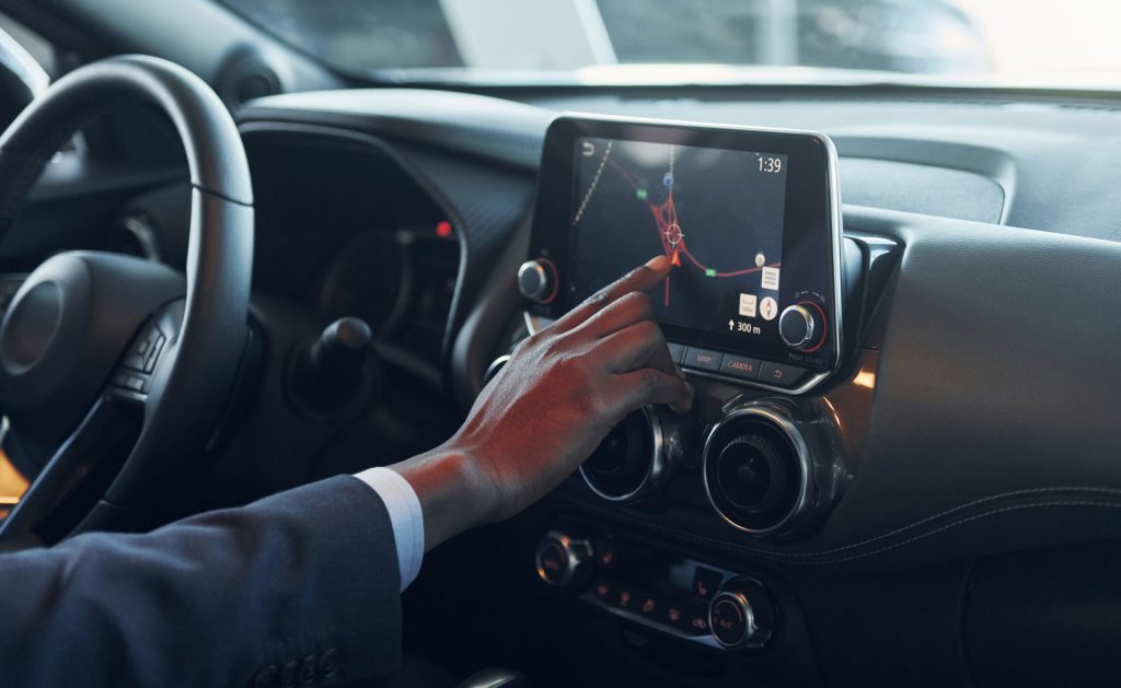 Using front control panel. Young african american businessman in black suit is in the automobile