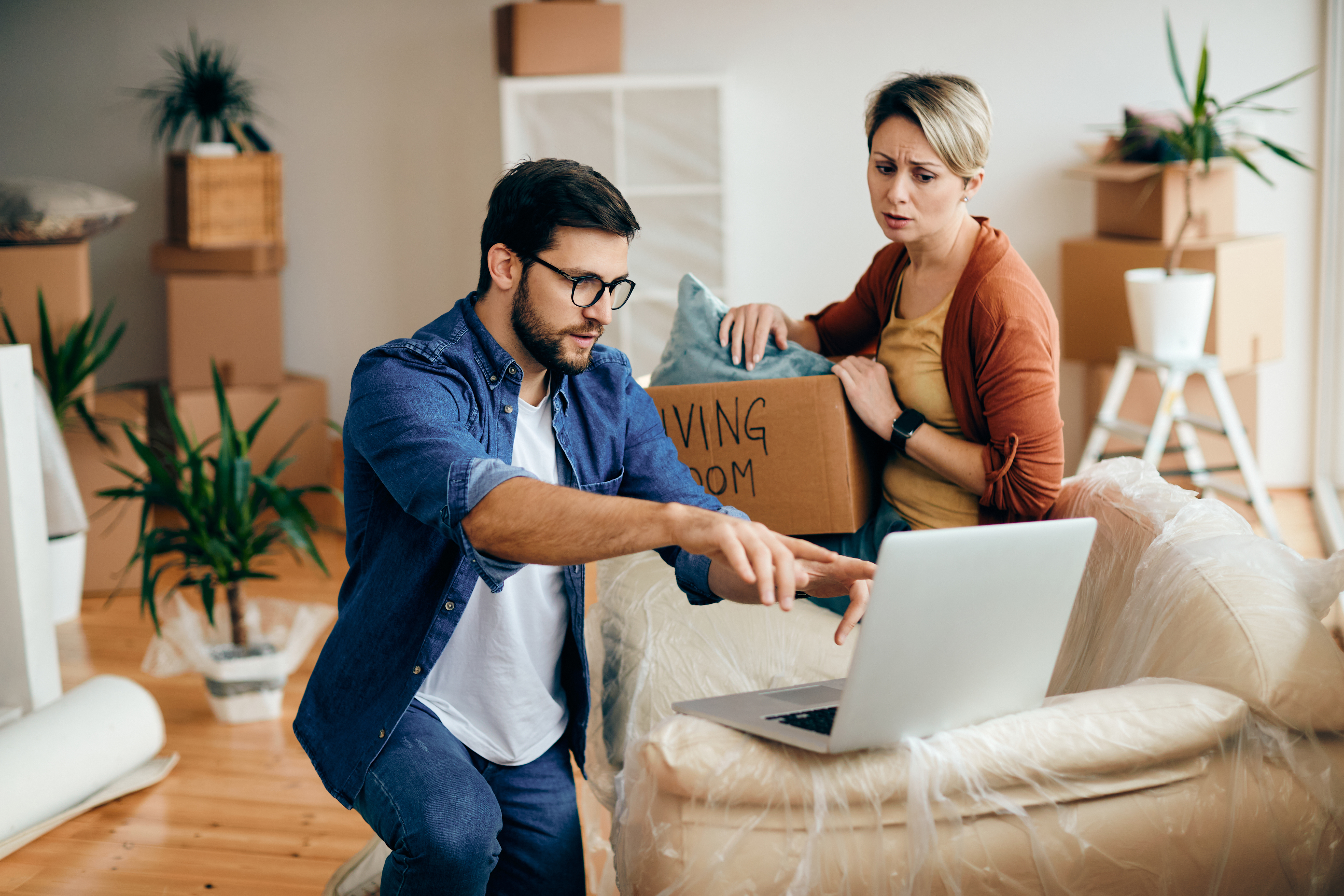 Distraught couple using laptop while moving into their new home.