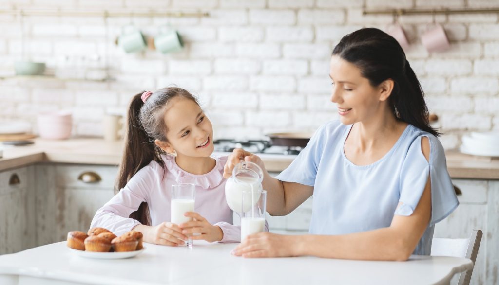 Beautiful mom and daughter drinking milk in kitchen together