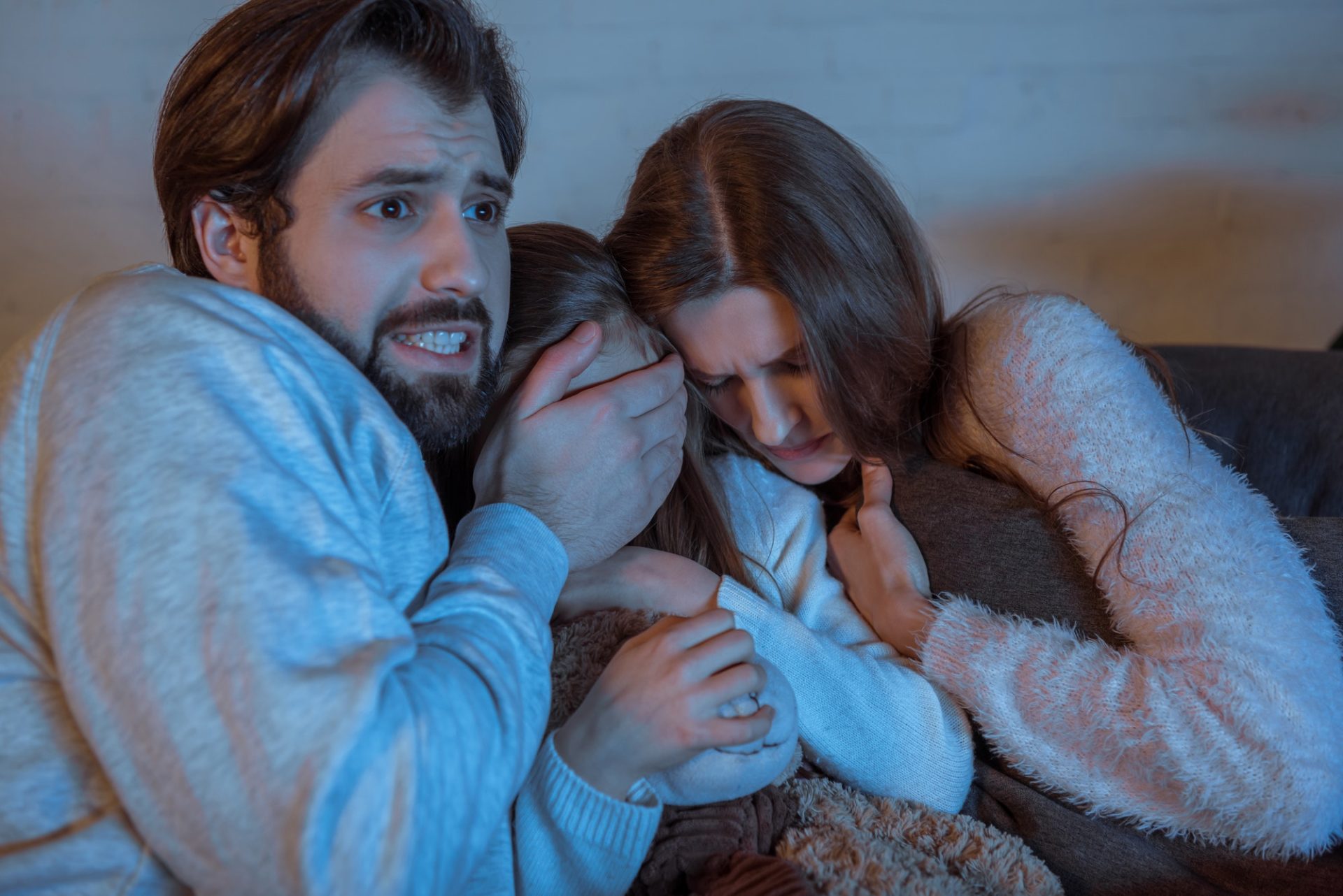 parents and daughter watching horror movie in evening