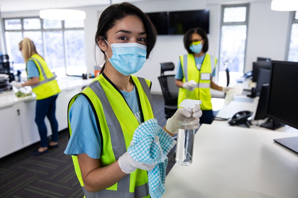 Portrait of woman wearing hi vis vest and face mask holding cleaning cloth and disinfectant