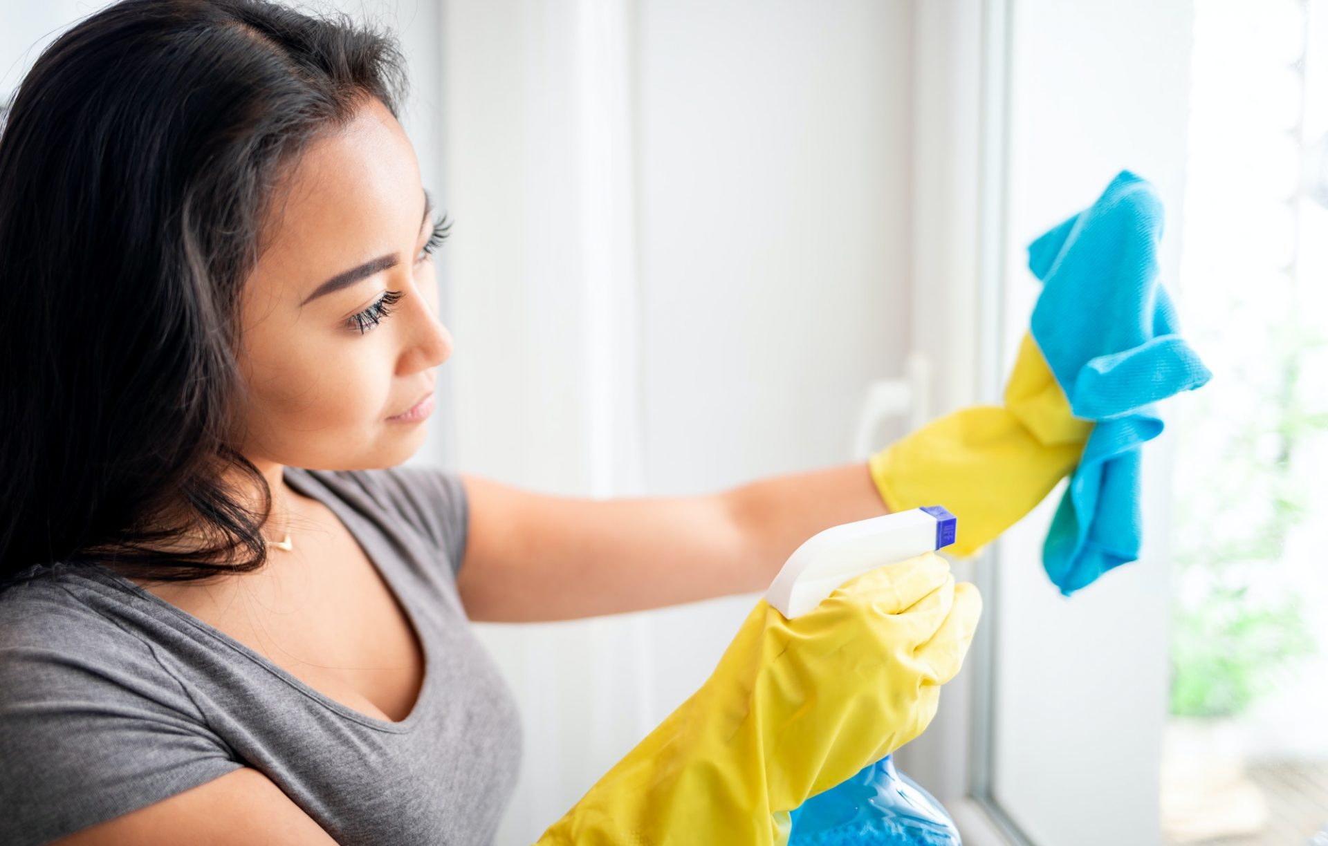 Young asian girl with gloves and spray cleaning windows