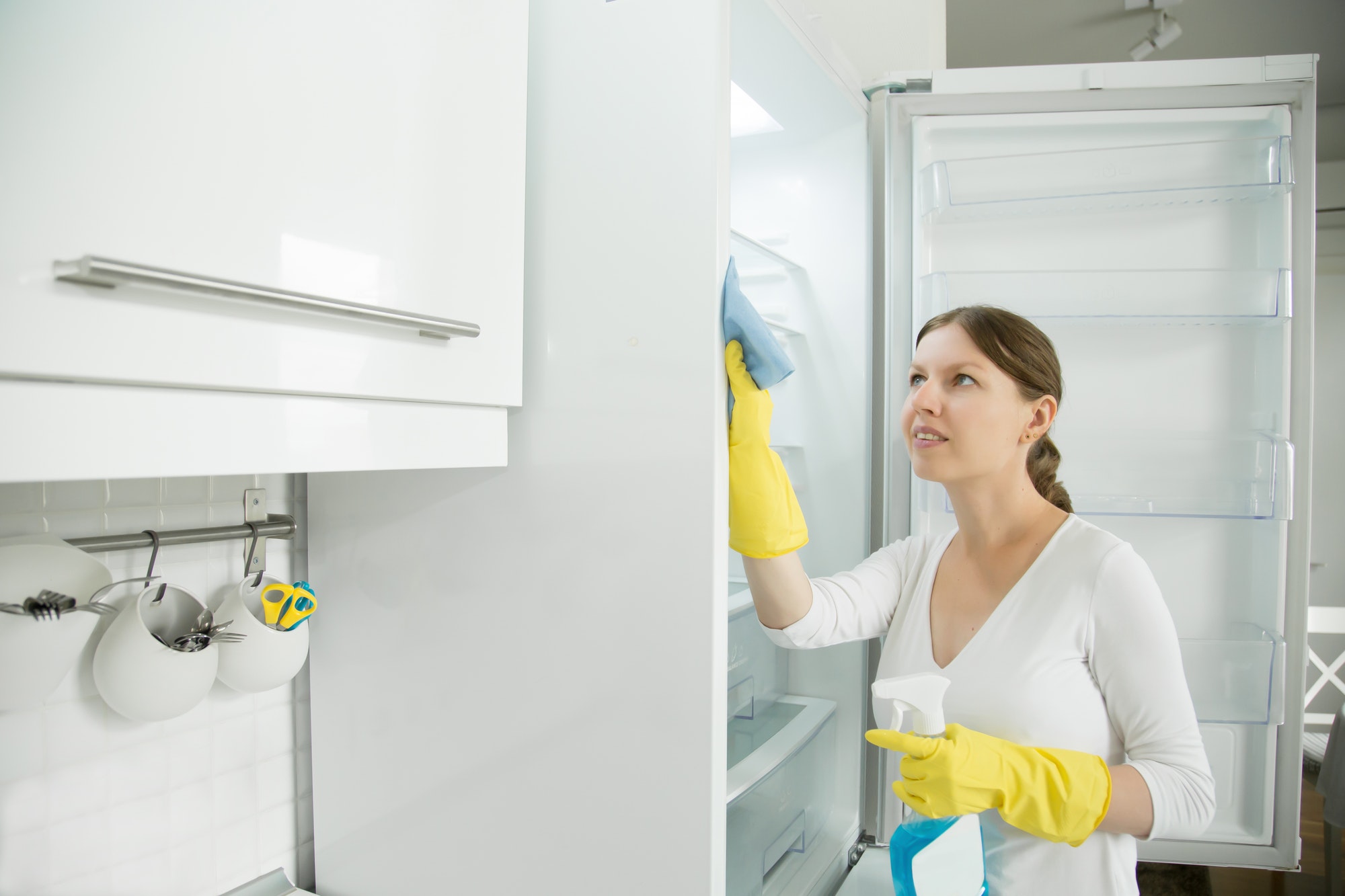 Young woman wearing rubber gloves cleaning the fridge