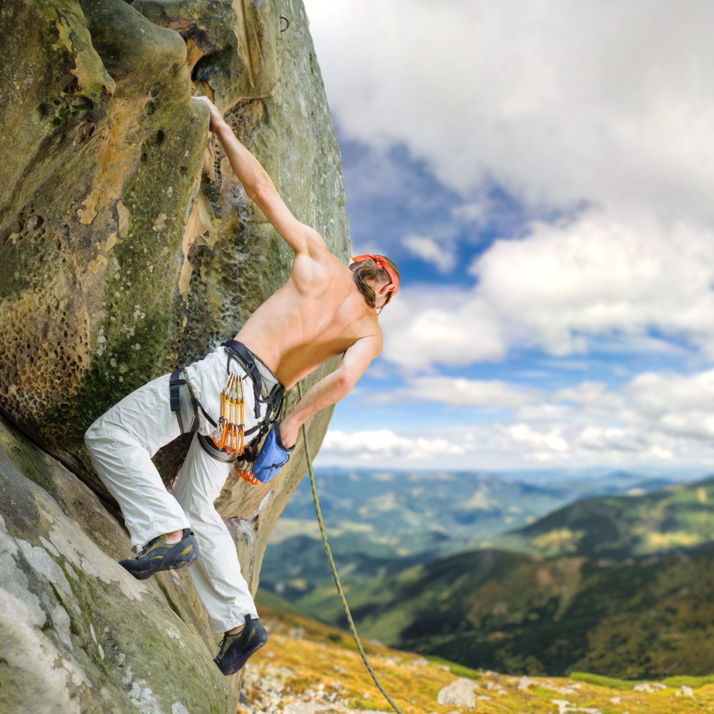 Male rock climber climbing with rope on a rocky wall