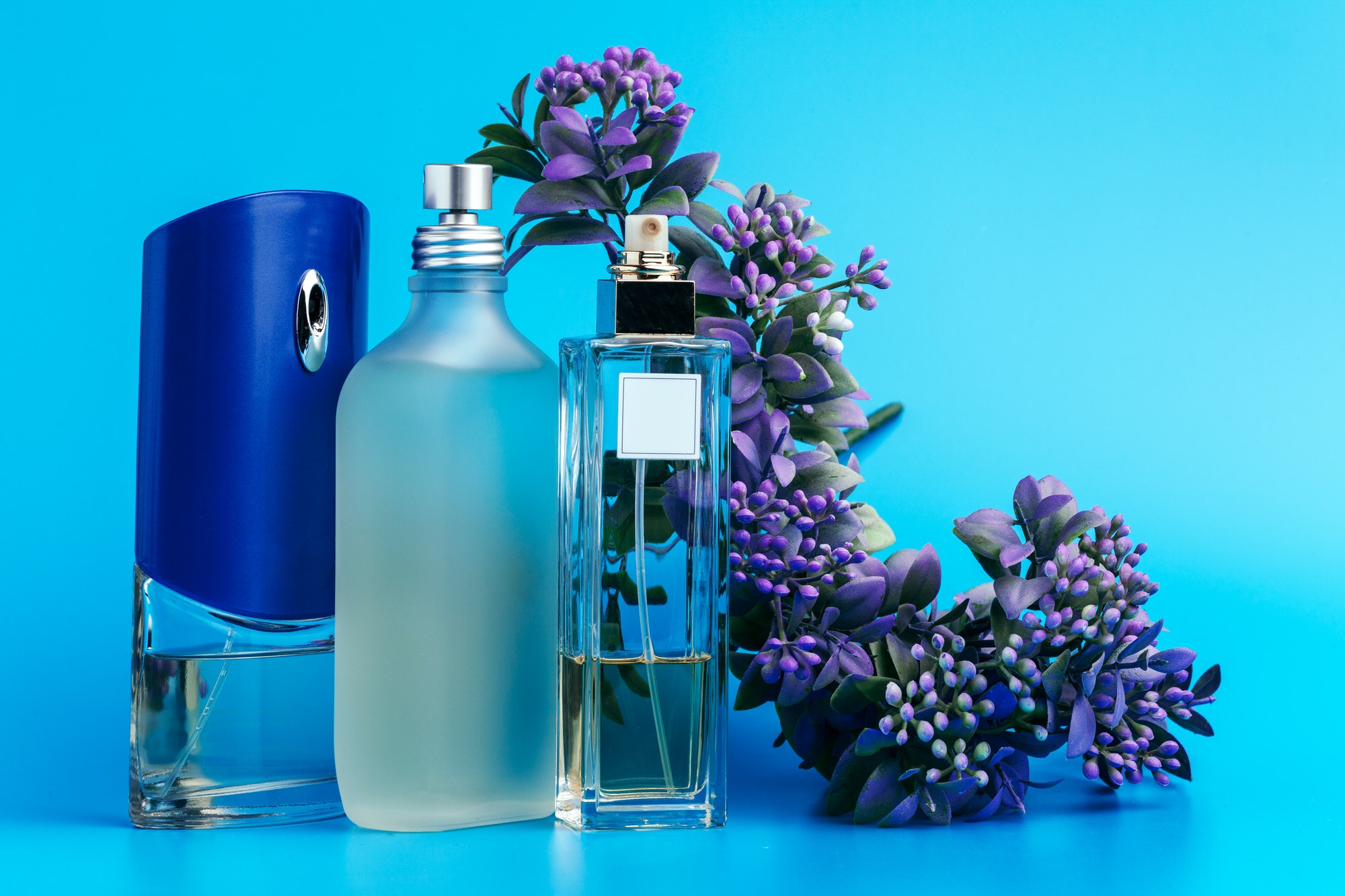 Perfume bottles with flowers on a light blue background