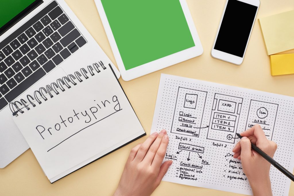 cropped view of designer holding website design template near gadgets and notebook with prototyping