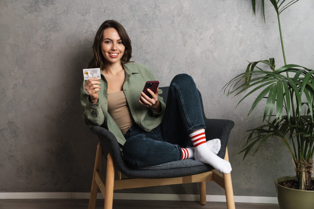 Smiling nice girl holding credit card and using cellphone