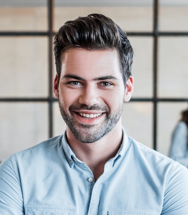 handsome young businessman with crossed arms smiling at camera in office