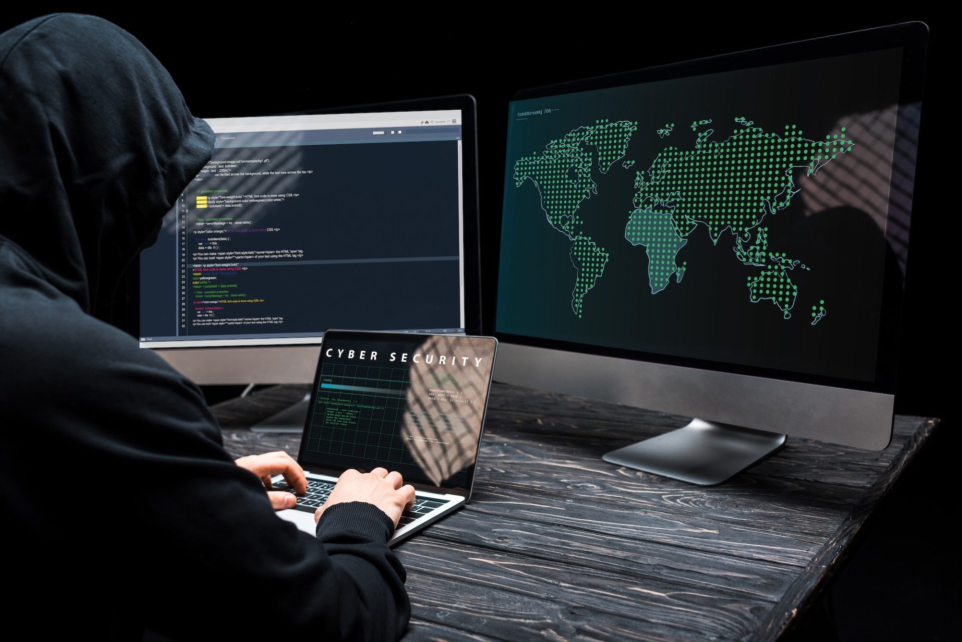 hacker using laptop with cyber security lettering on screen near computer monitors on black