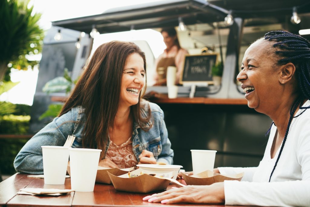 Happy multiracial senior women eating at food truck restaurant outdoor