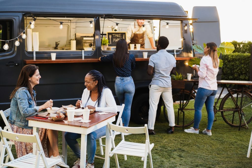 Multiracial people having fun eating at food truck restaurant - Focus on african woman face