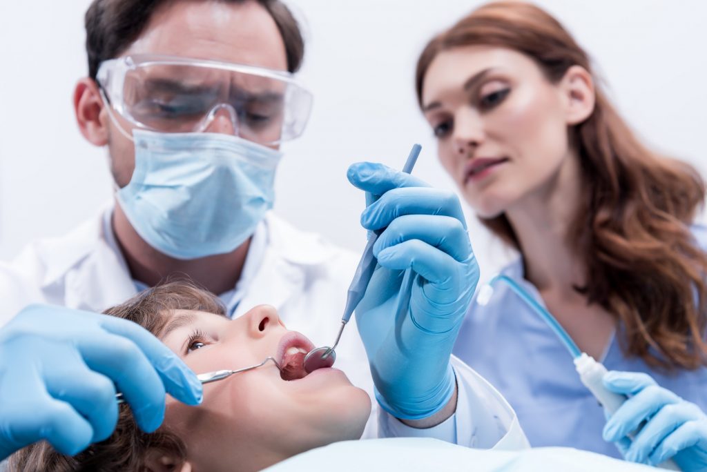 low angle view of dentists examining teeth of little boy at dentist office