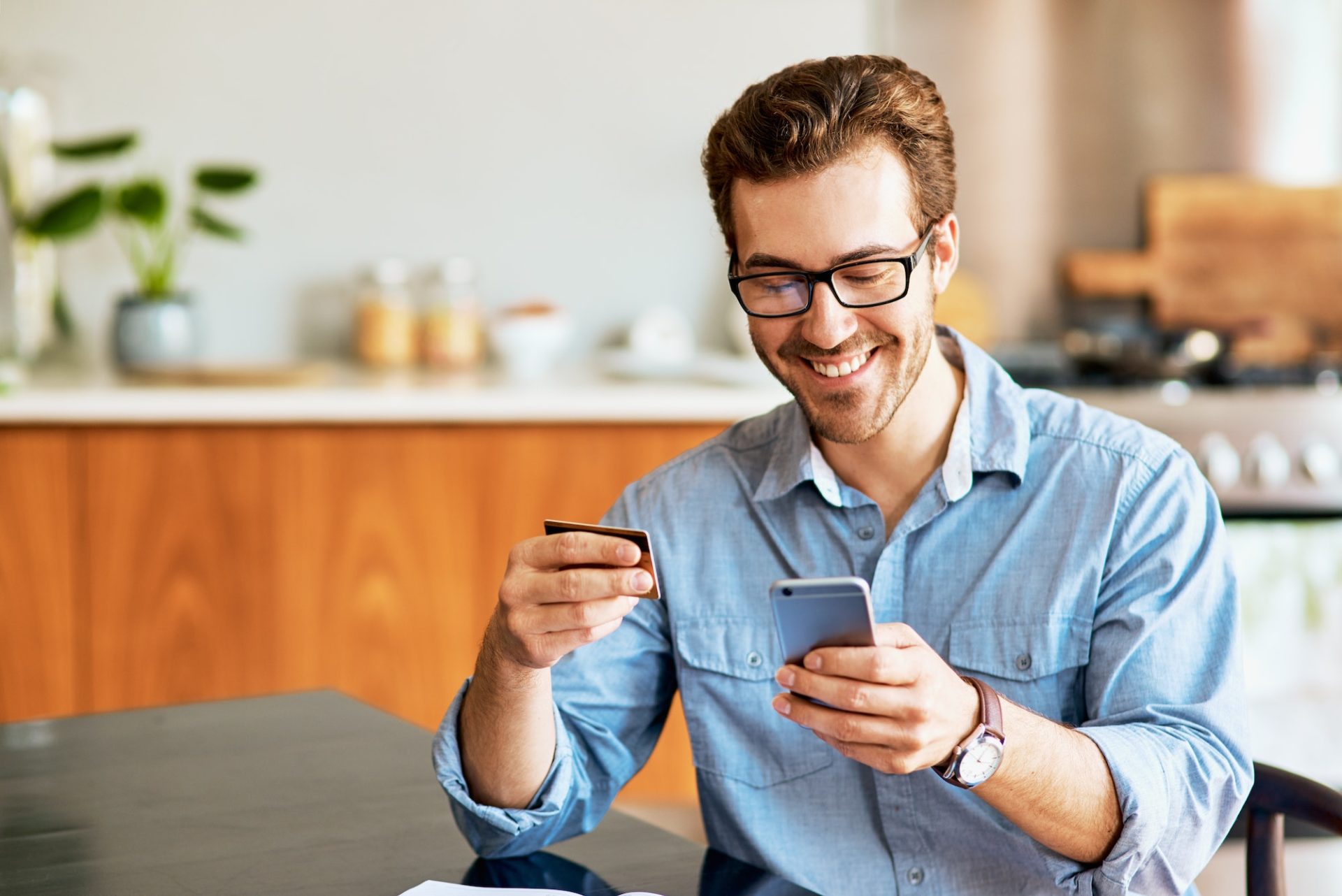 Shot of a handsome young man using a cellphone and credit card at home