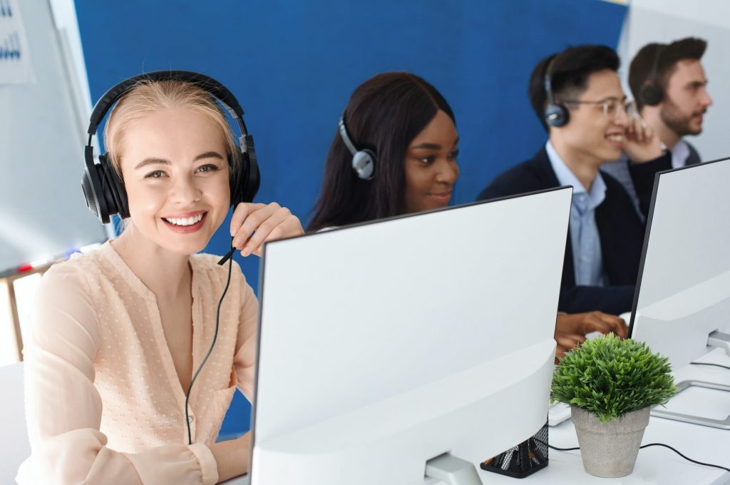 Joyful customer service agents with headphones communicating with clients at call center