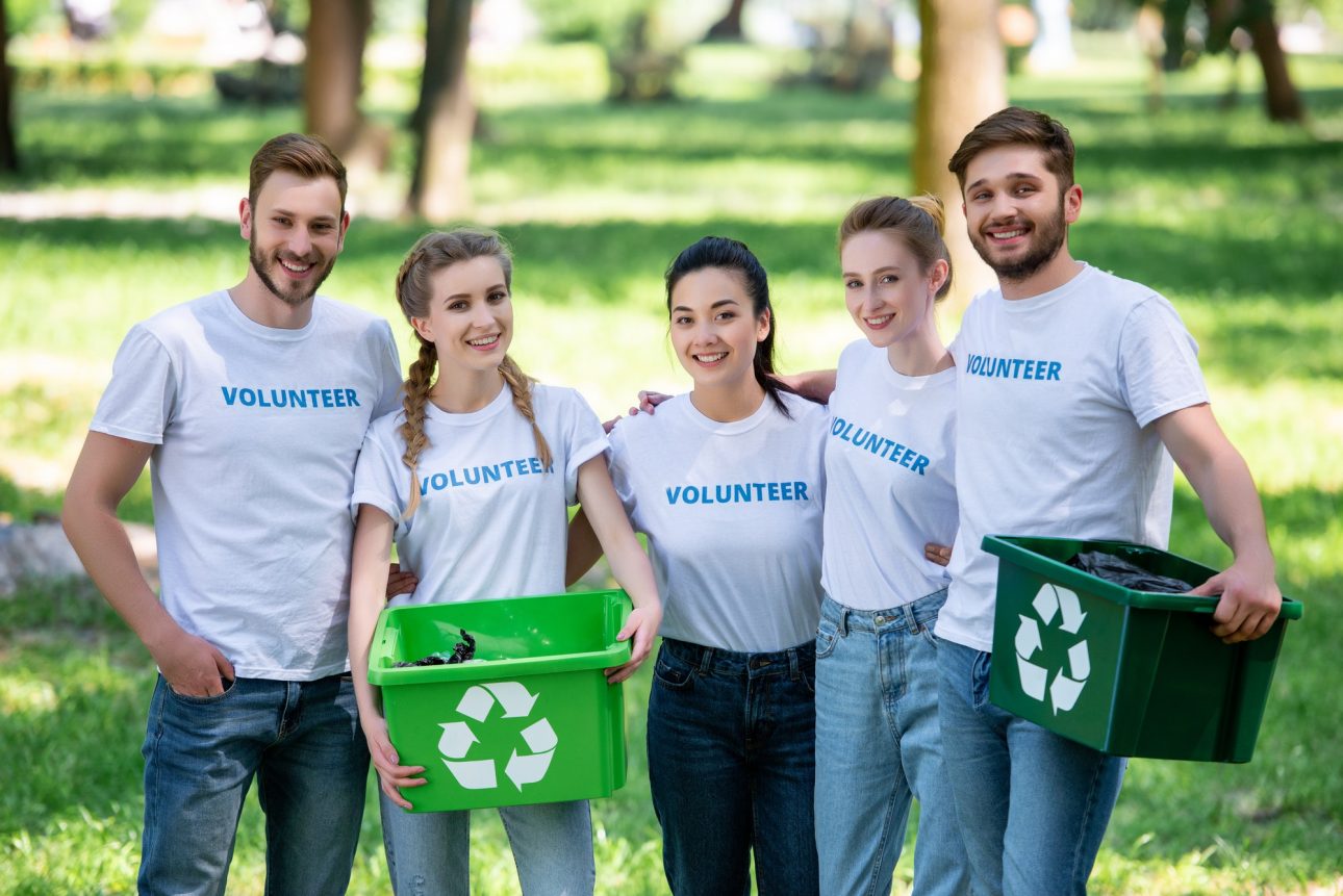 young volunteers with green recycling boxes for trash standing in park