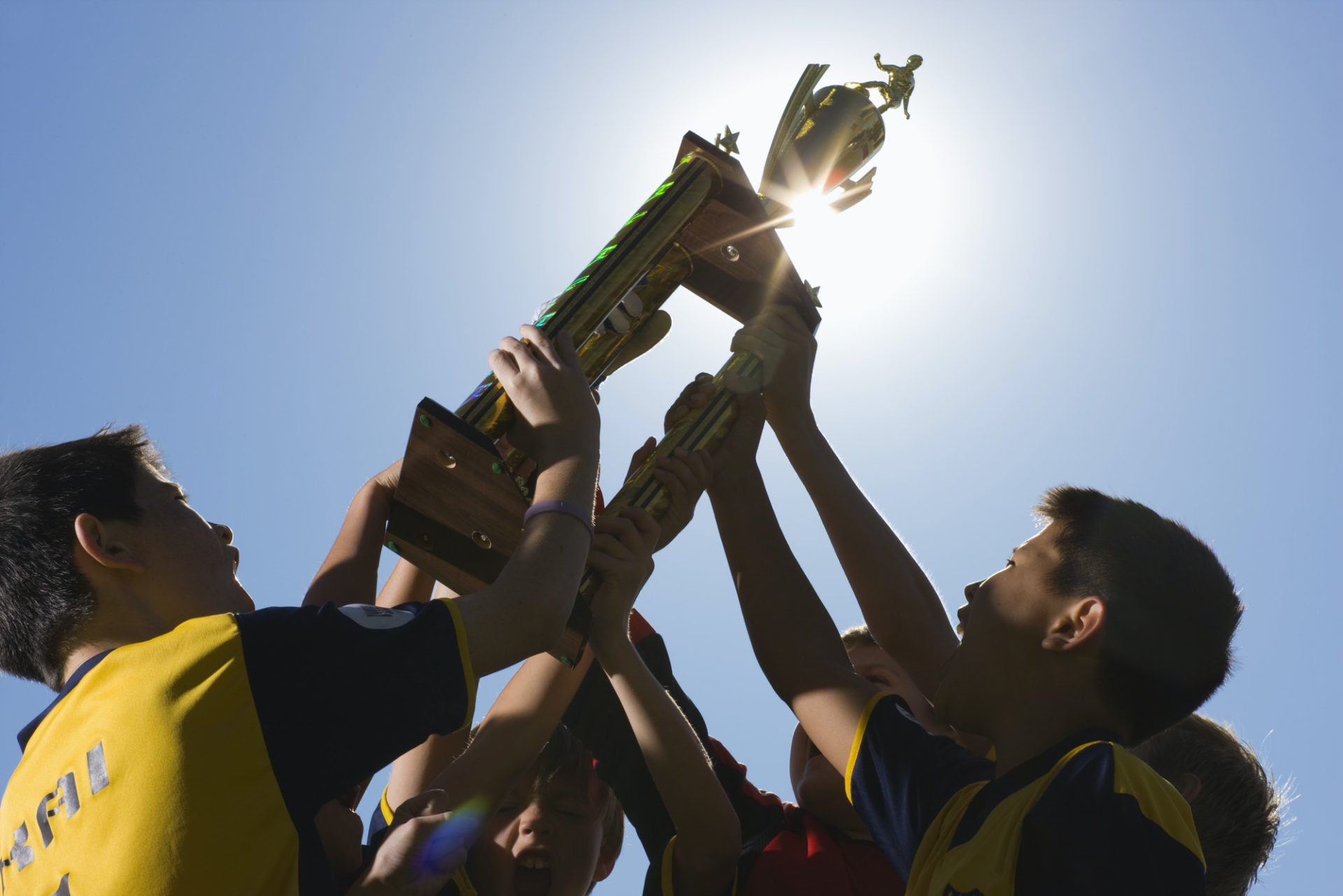 A group of boys in soccer team shirts holding a trophy and celebrating a win.