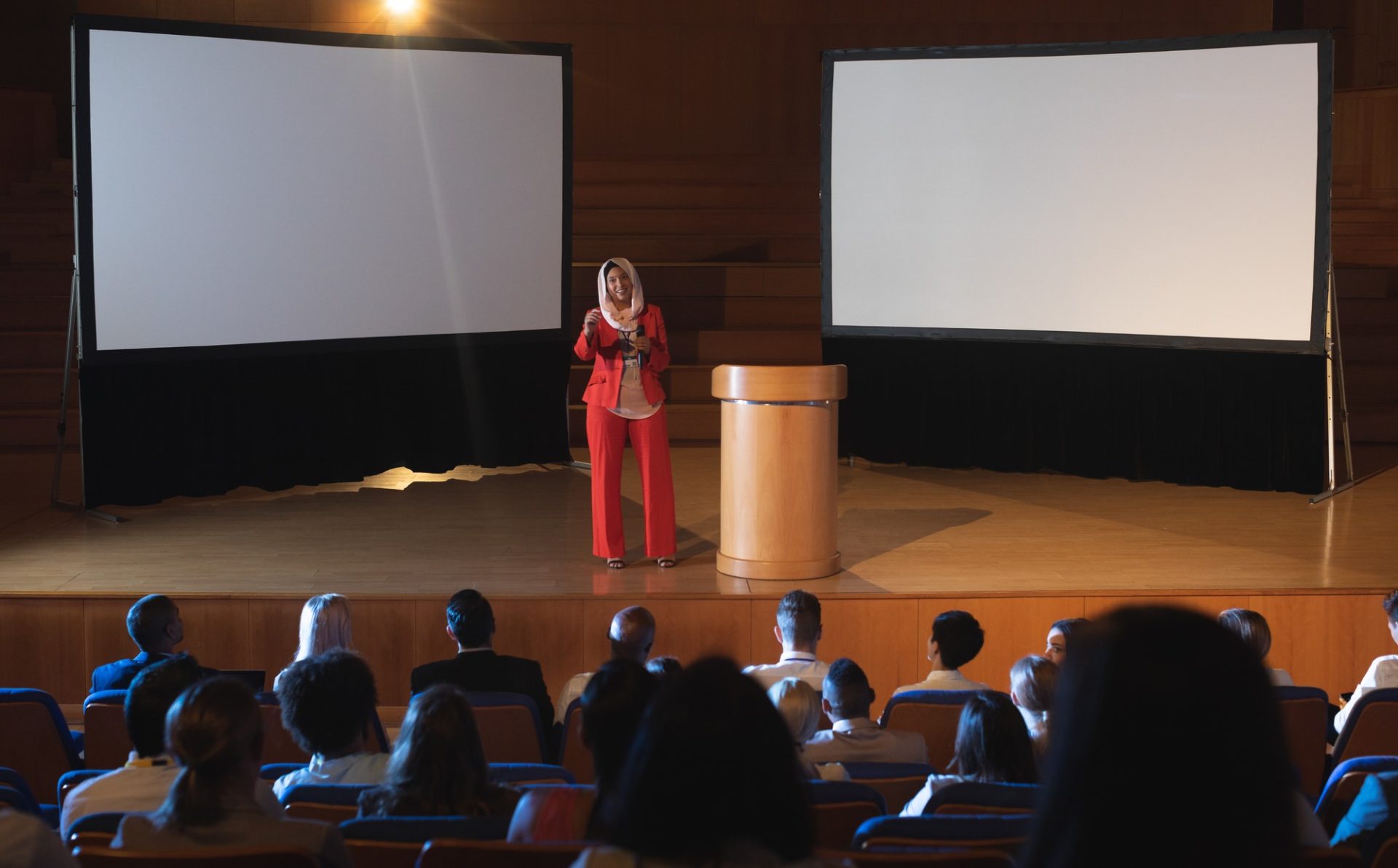 Businesswoman standing near podium and giving presentation to the audience in auditorium