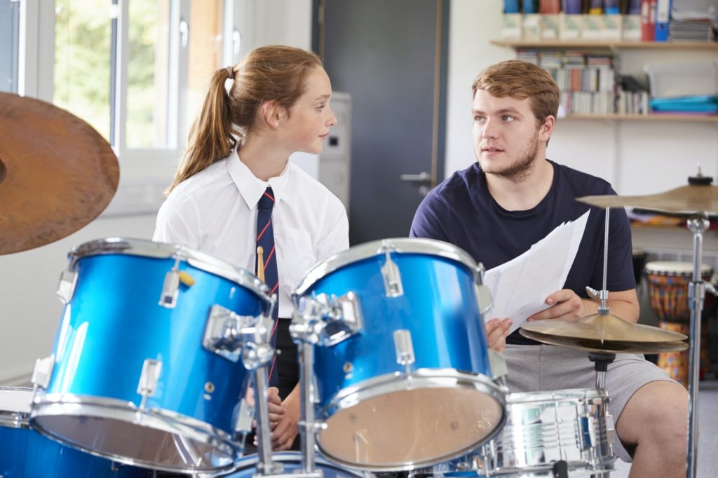 Female Pupil With Teacher Playing Drums In Music Lesson