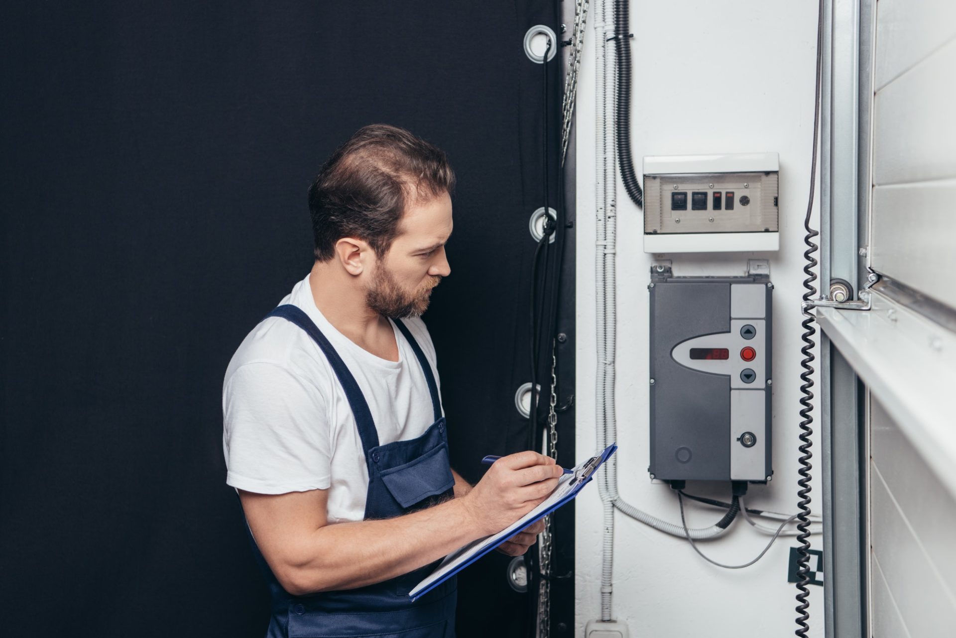 male electrician writing in clipboard and checking electrical box