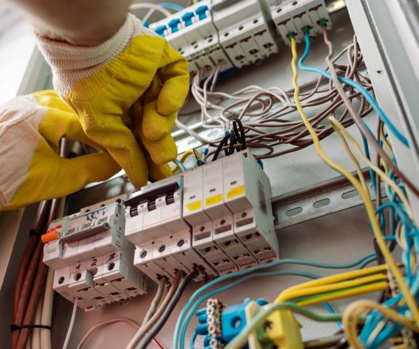 Low angle view of electrician in gloves fixing electrical distribution box