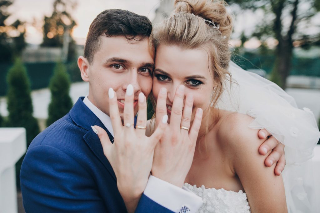 Just married. Stylish happy bride and groom showing hands with wedding rings
