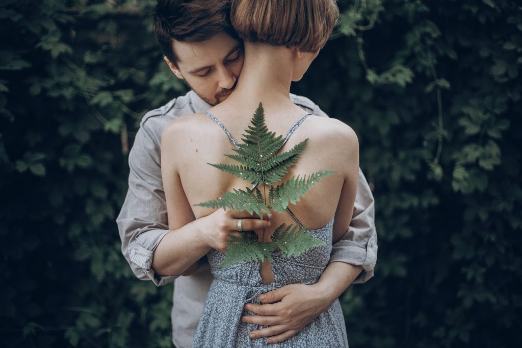 Stylish hipster bride and groom embracing in green leaves forest. man kissing woman neck