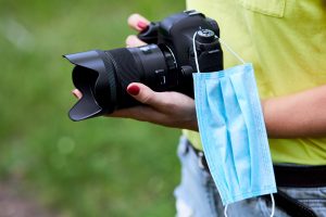 Woman photographer with a photo camera in hand outdoor with protection mask