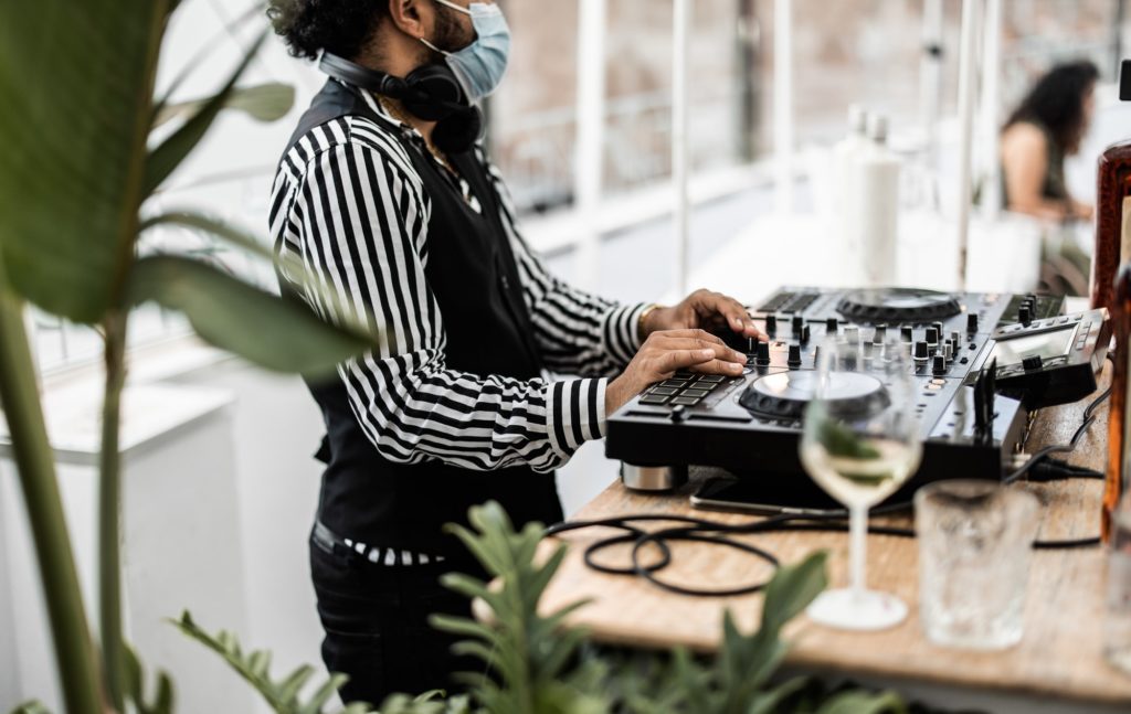 African dj playing music at cocktail bar outdoor while wearing face safety mask