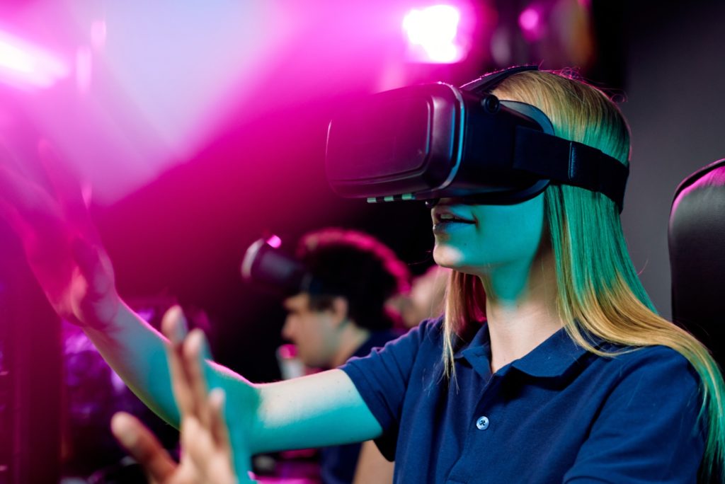 Blond girl in vr goggle touching virtual display during cybersports video game