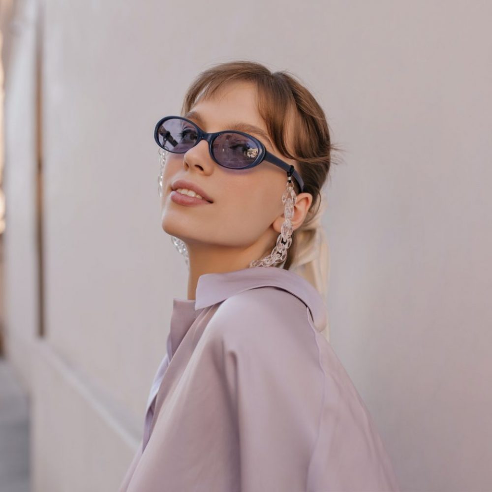 Close-up portrait of young girl in city. Pretty brunette wearing silk outfit, purple sunglasses wit