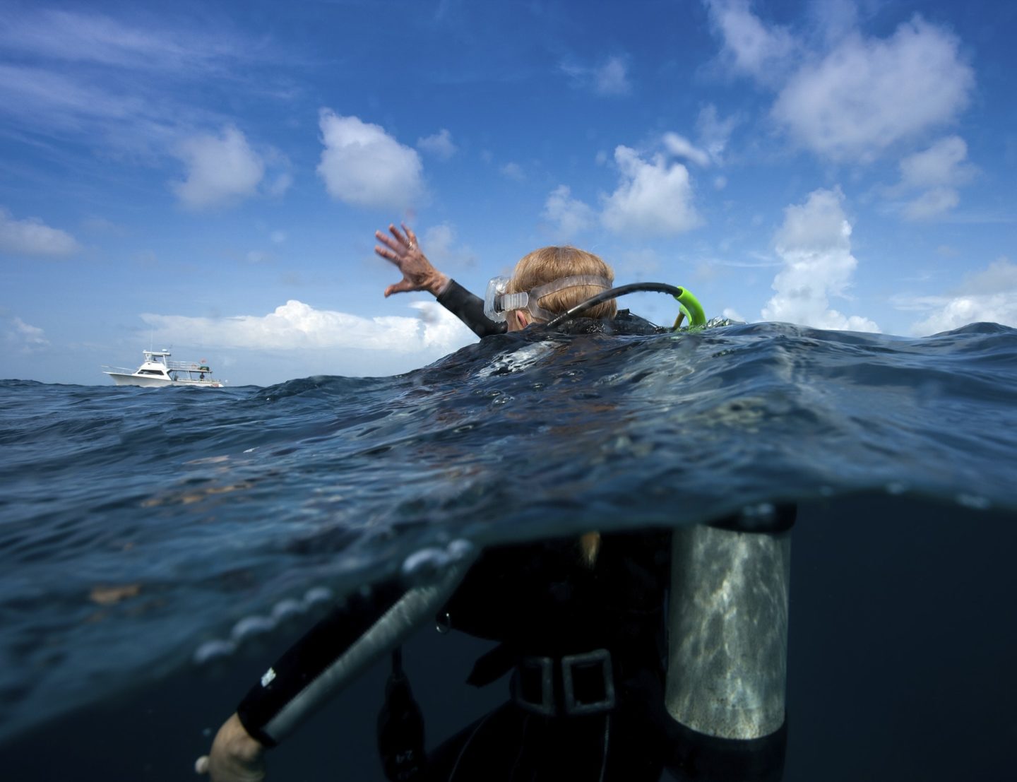 Scuba diver waves one arm to show distress and that she requires assistance.