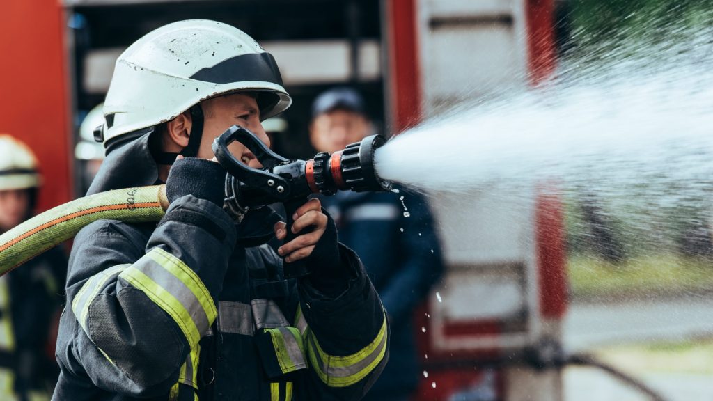 selective focus of firefighter with water hose extinguishing fire on street