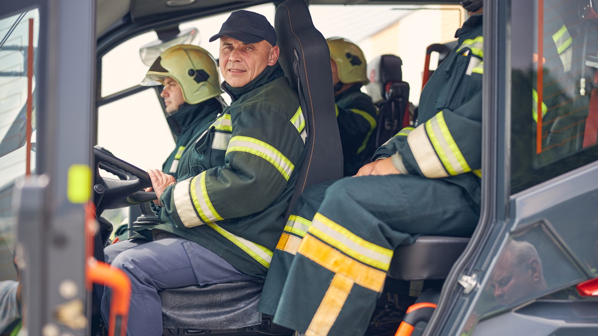 Senior man sitting in the fire truck with group of firefighter