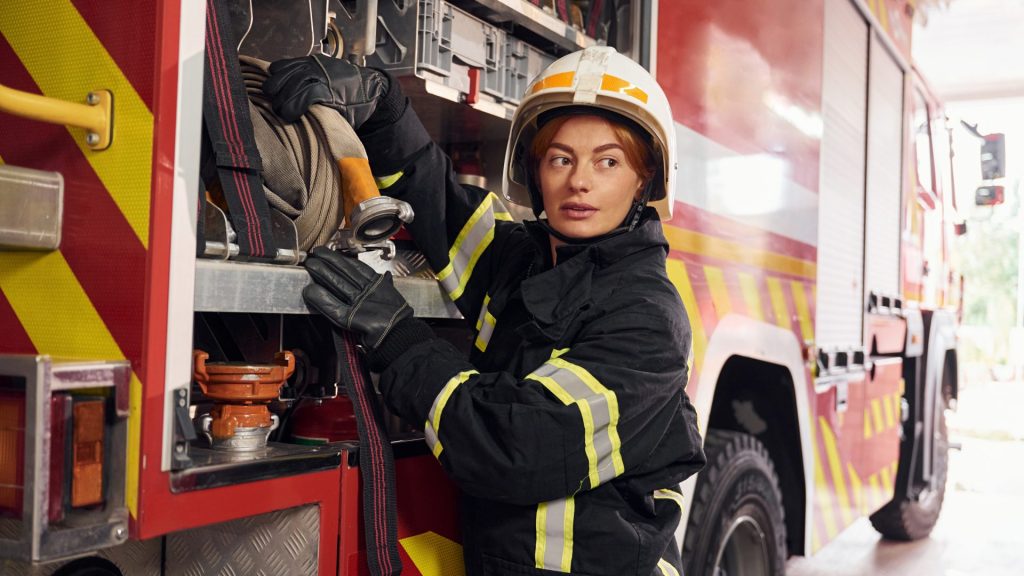 Taking equipment from the truck. Woman firefighter in uniform is at work in department