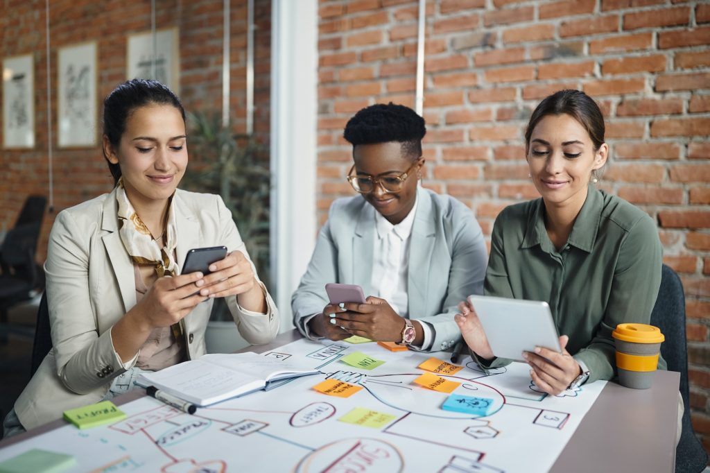 Multiracial group of happy businesswomen using wireless technology while working in the office.