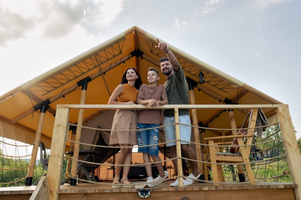 Happy family standing by glamping house in natural environment