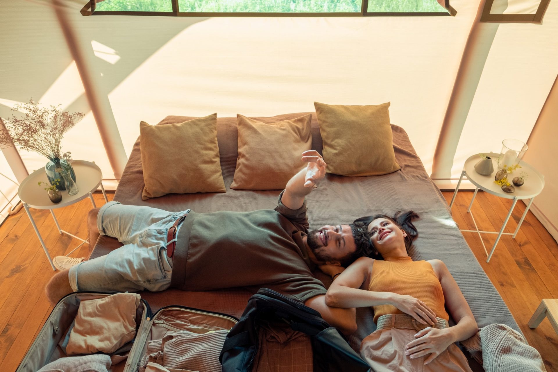 Happy idyllic couple relaxing on large bed in glamping house