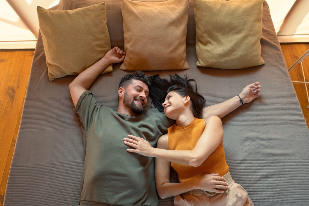 Young restful couple lying on bed with three cushions